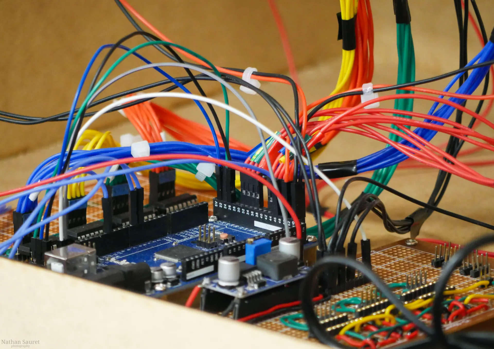Gros plan sur un Arduino Mega posé sur une plaque à pastilles, entouré de faisceaux de fils rouges, bleus, jaunes et verts.